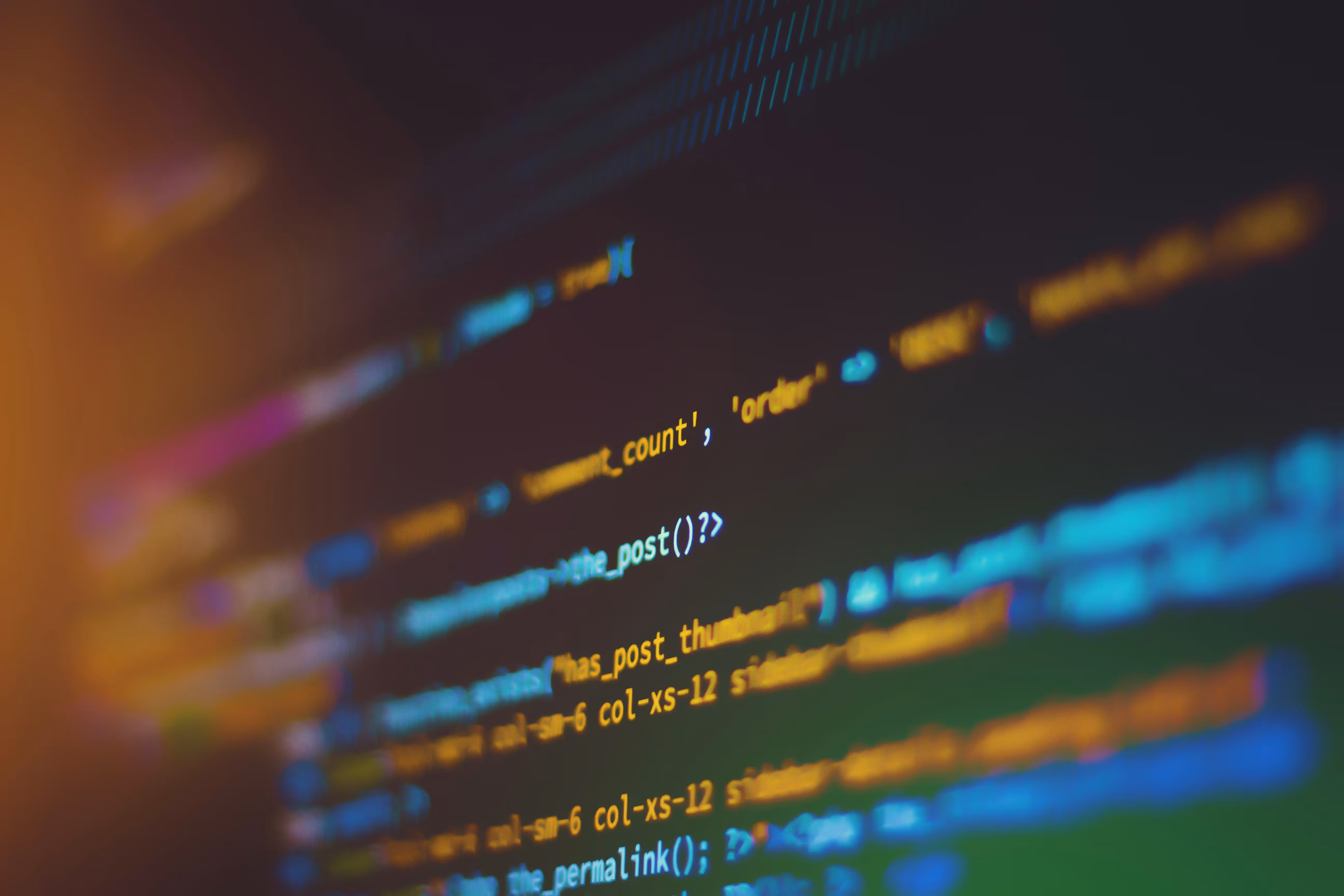 Blurry colorful lines of programming code on a dark screen with warm light on the left.