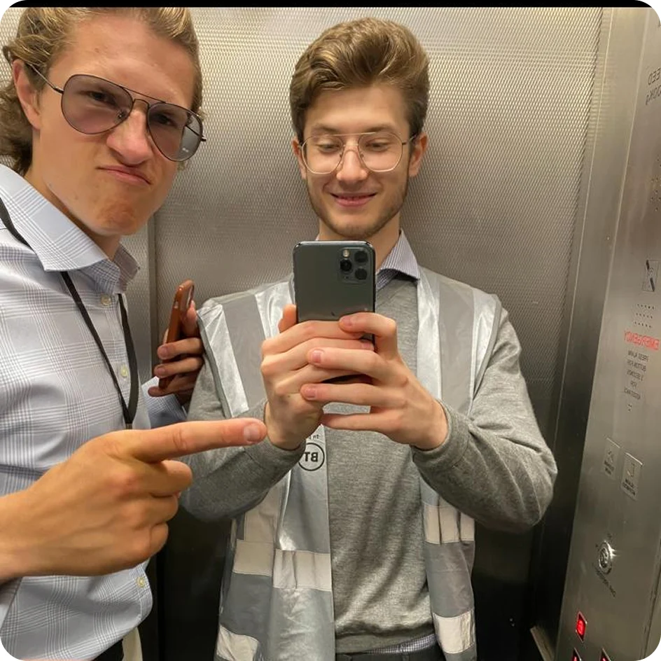 Two young men in an elevator taking a selfie, one pointing and making a playful face.