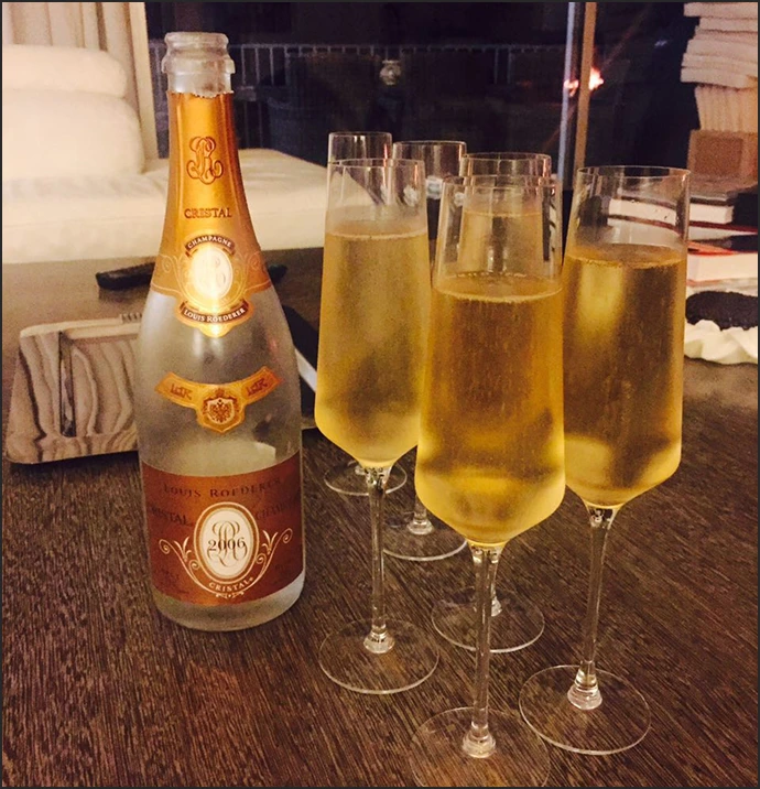 Bottle of Cristal champagne with four filled champagne flutes on a wooden table.