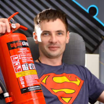 Man wearing a Superman logo t-shirt holding a red fire extinguisher.