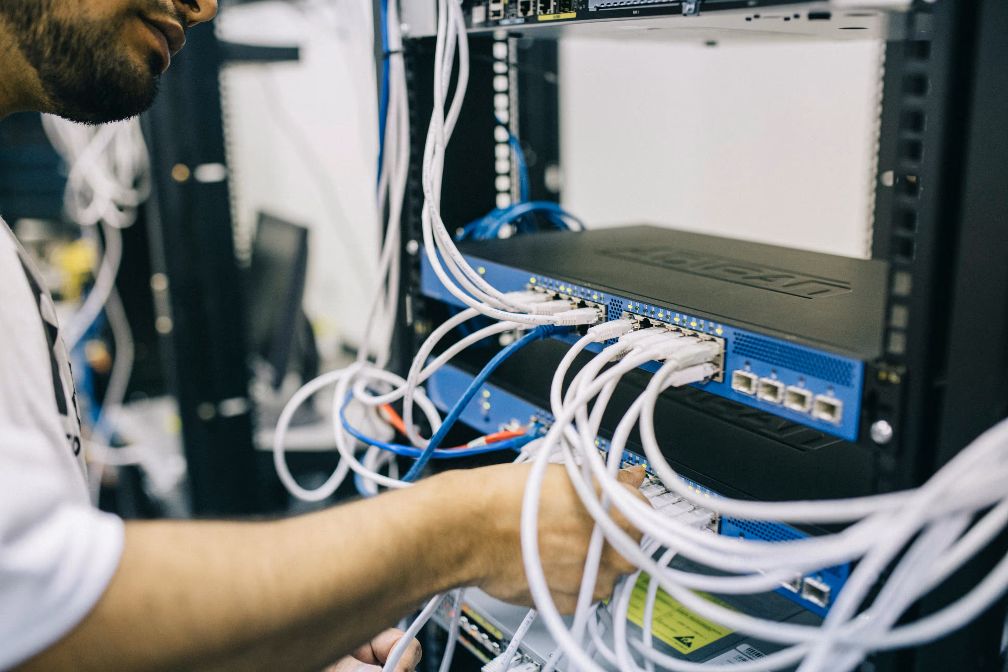 Technician working on network switches with multiple connected Ethernet cables in a server rack.