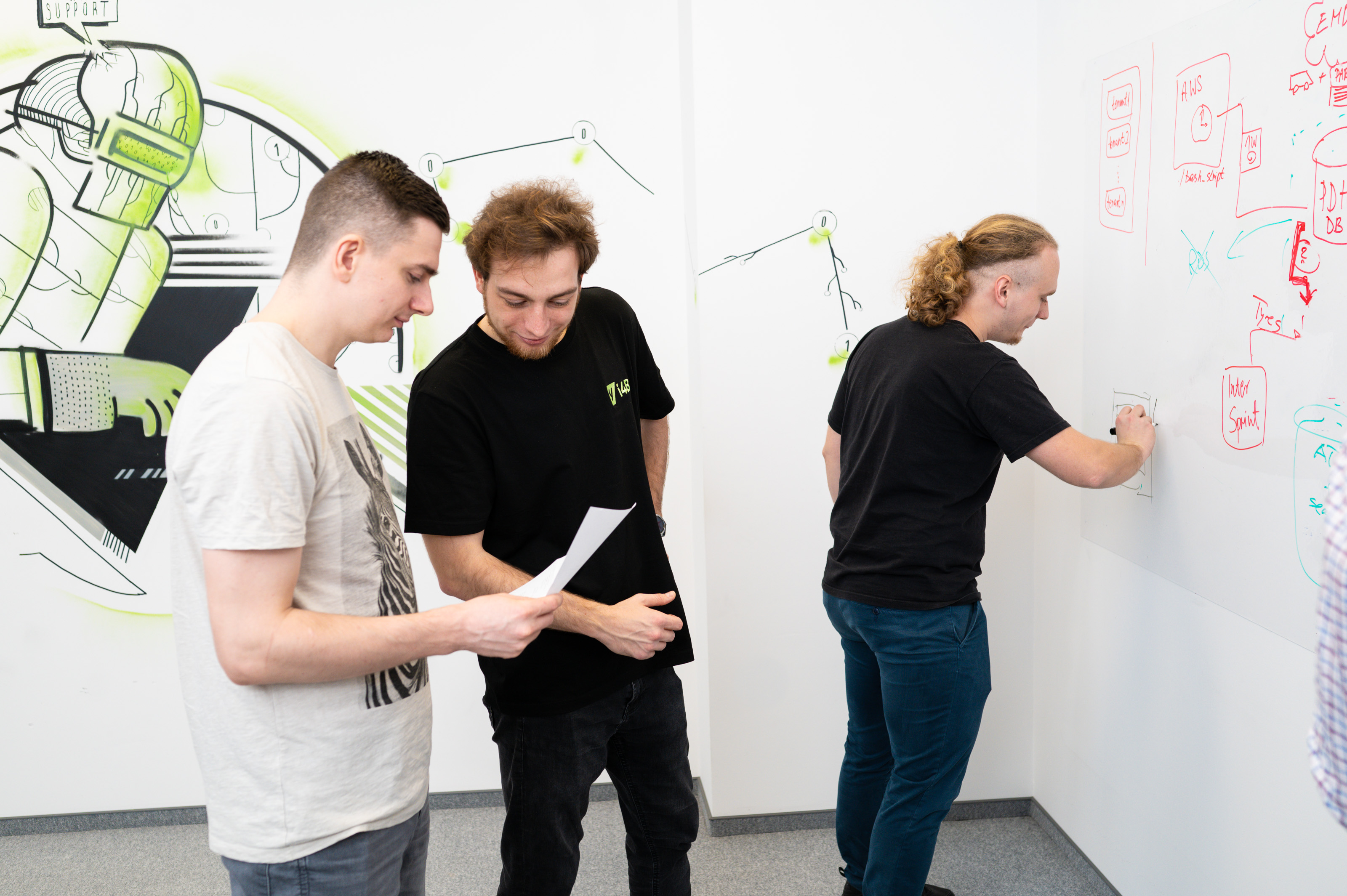 Three men brainstorming in a room with a whiteboard and graffiti art on the walls.