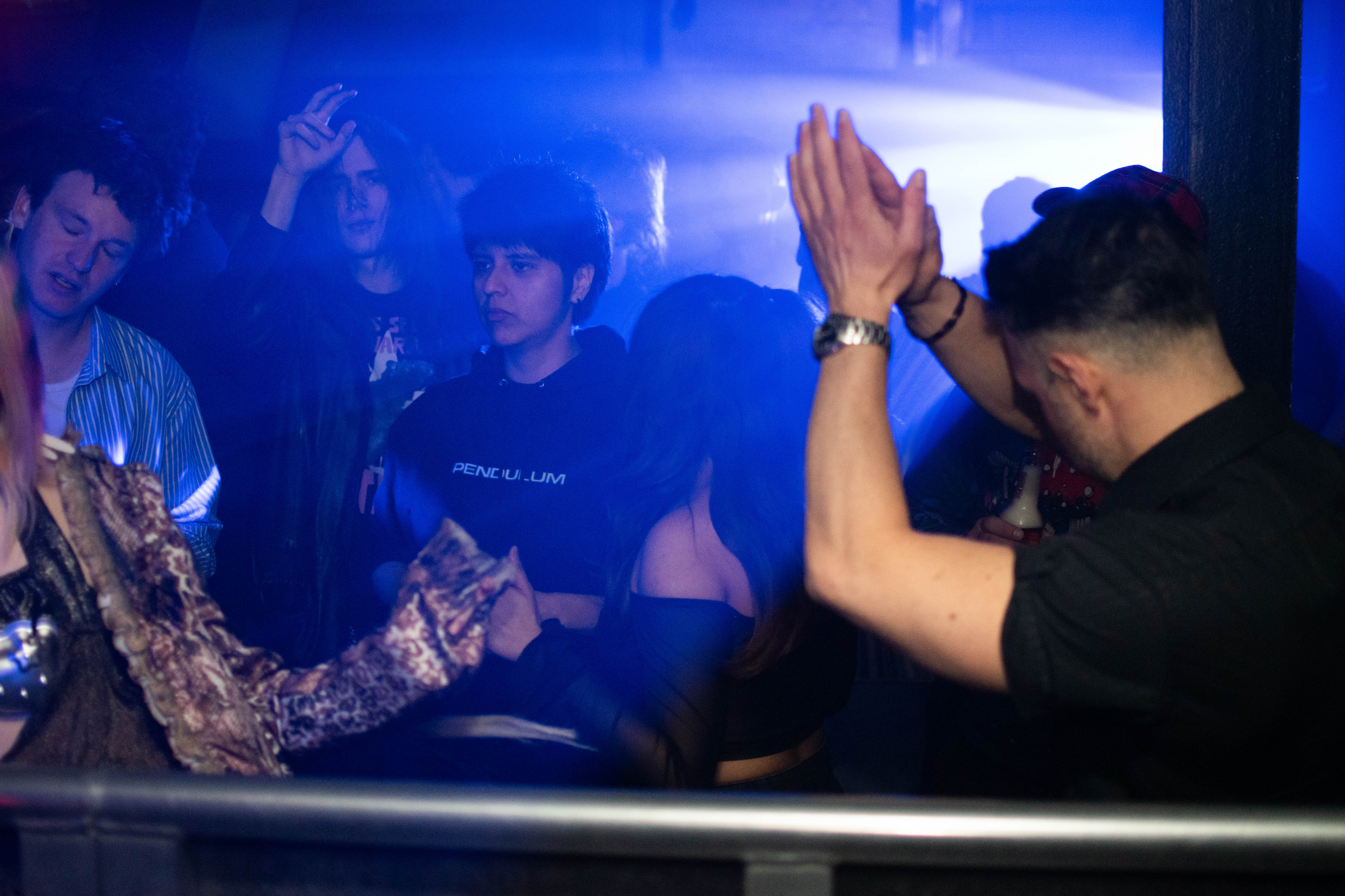 Group of people dancing and socializing in a dim club with blue lighting and fog effects.