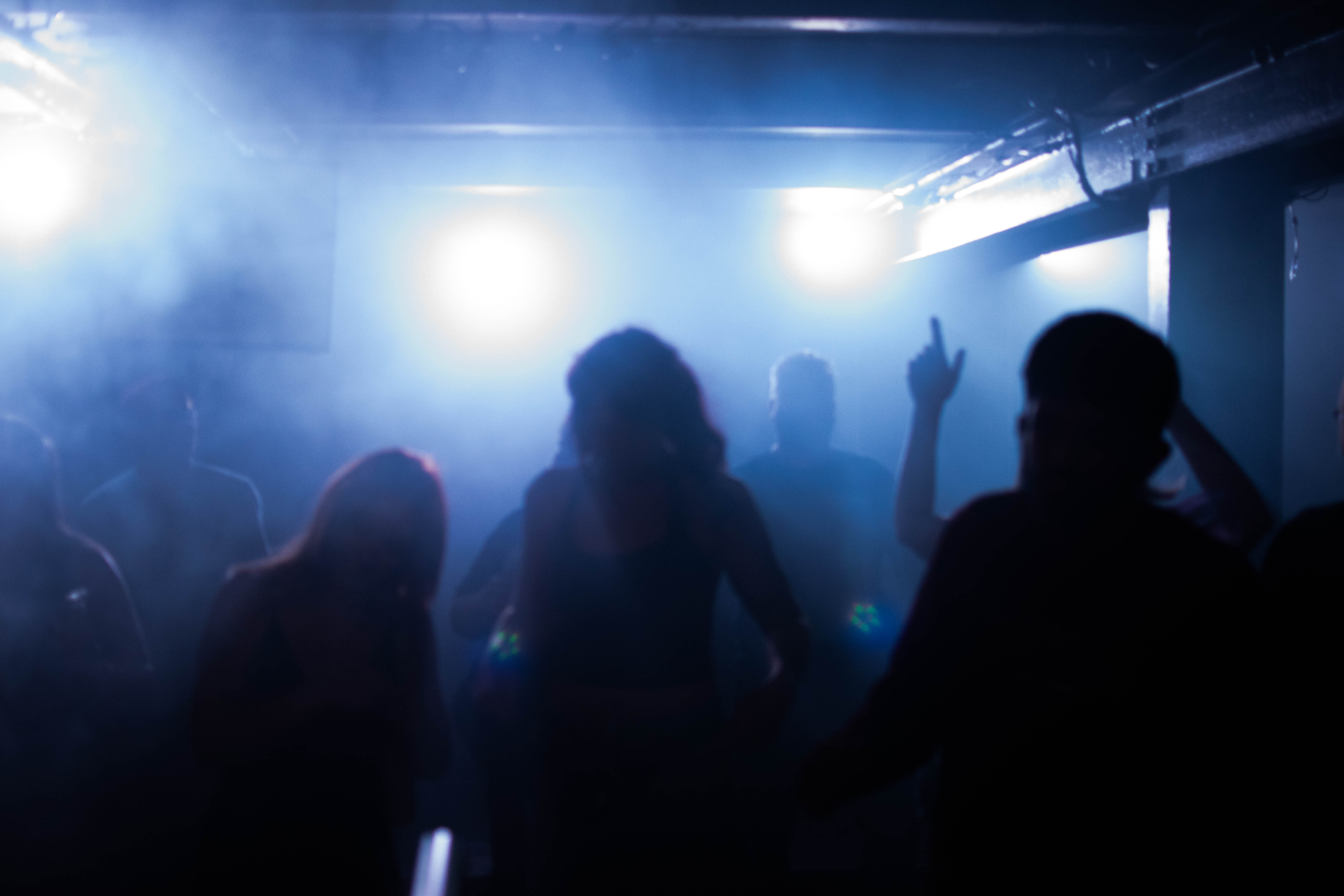 Silhouettes of people dancing in a dim, foggy room with three bright lights in the background.