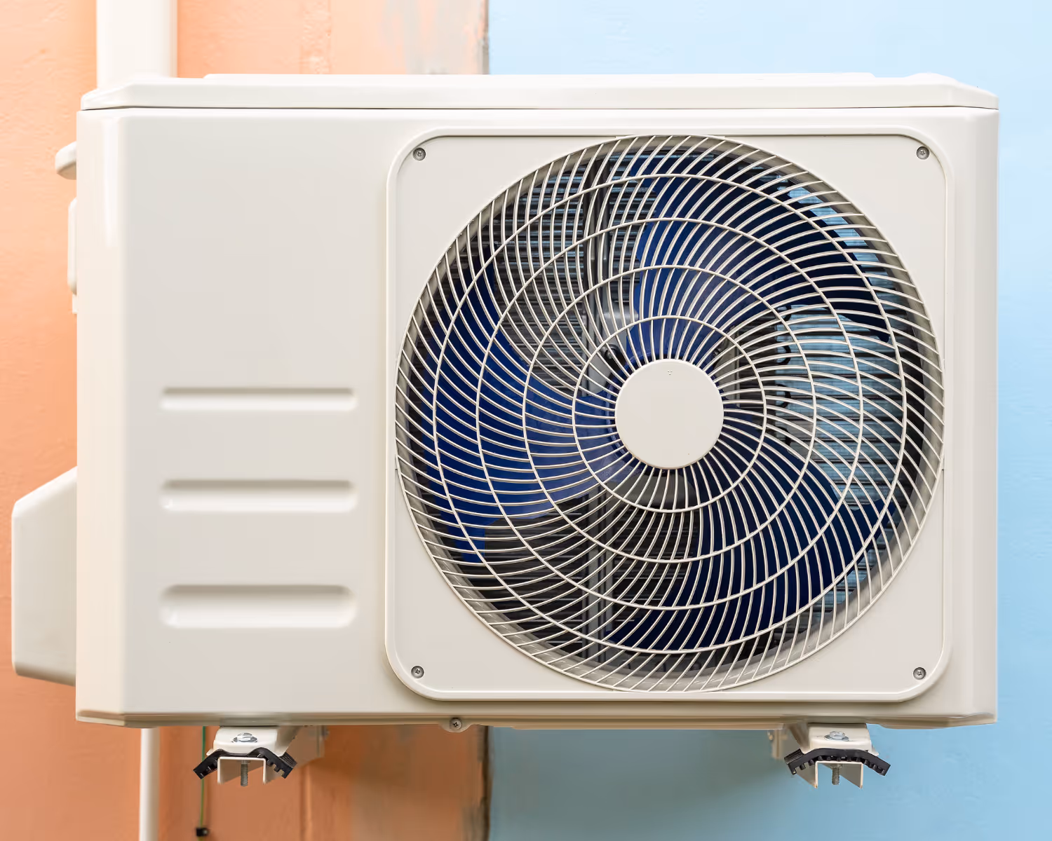 Outdoor unit of an air conditioning system mounted on a wall with a protective metal grille covering the fan.