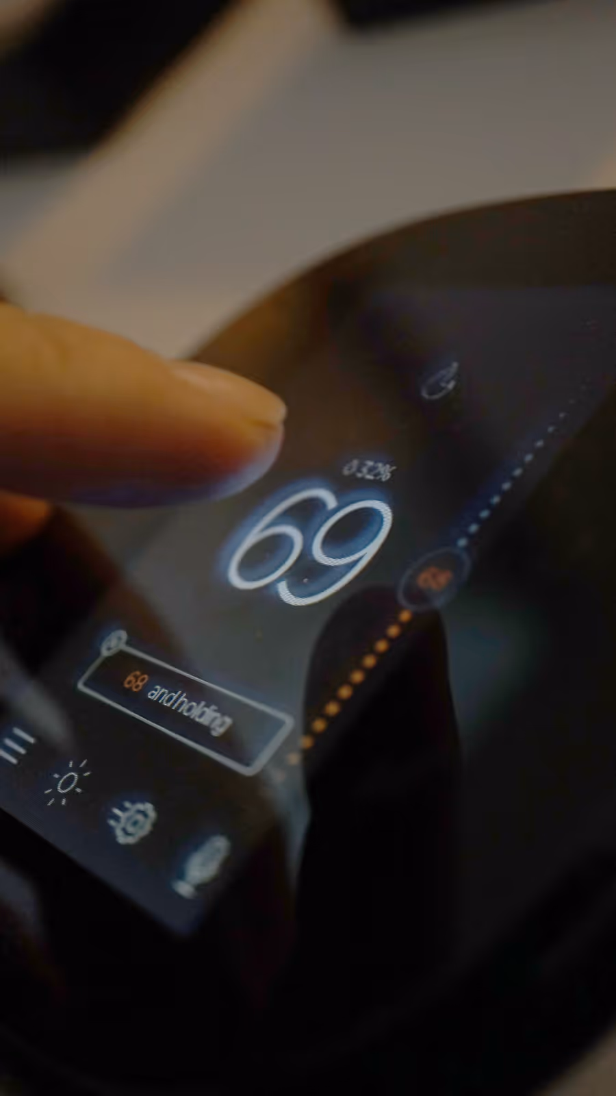 Close-up of a finger interacting with a smart thermostat display showing temperature set at 69 degrees and '68 and holding' message.