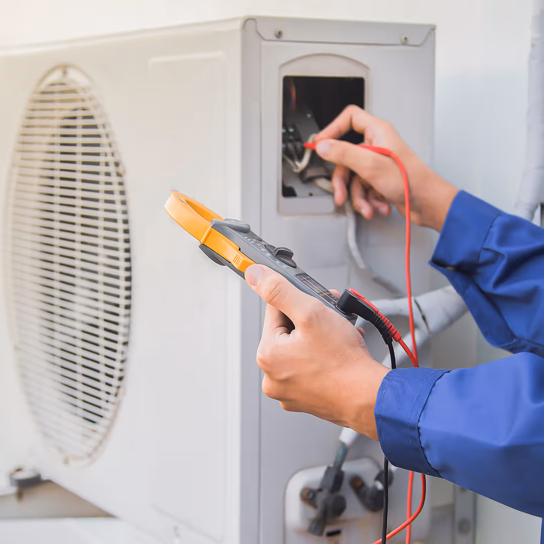 Technician in blue sleeves using a clamp meter to test an air conditioning unit.