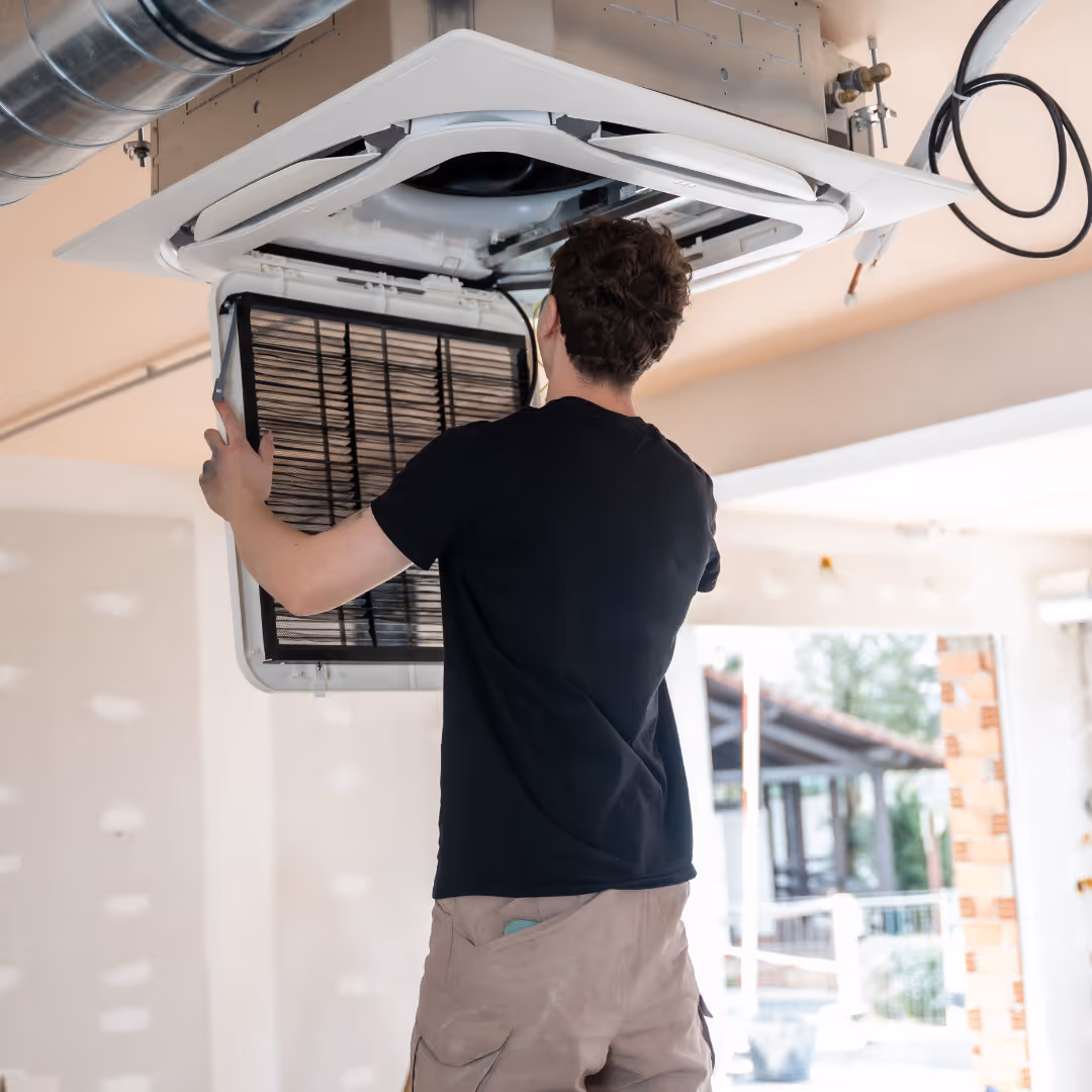 Technician performing maintenance on a ceiling-mounted air conditioning unit.