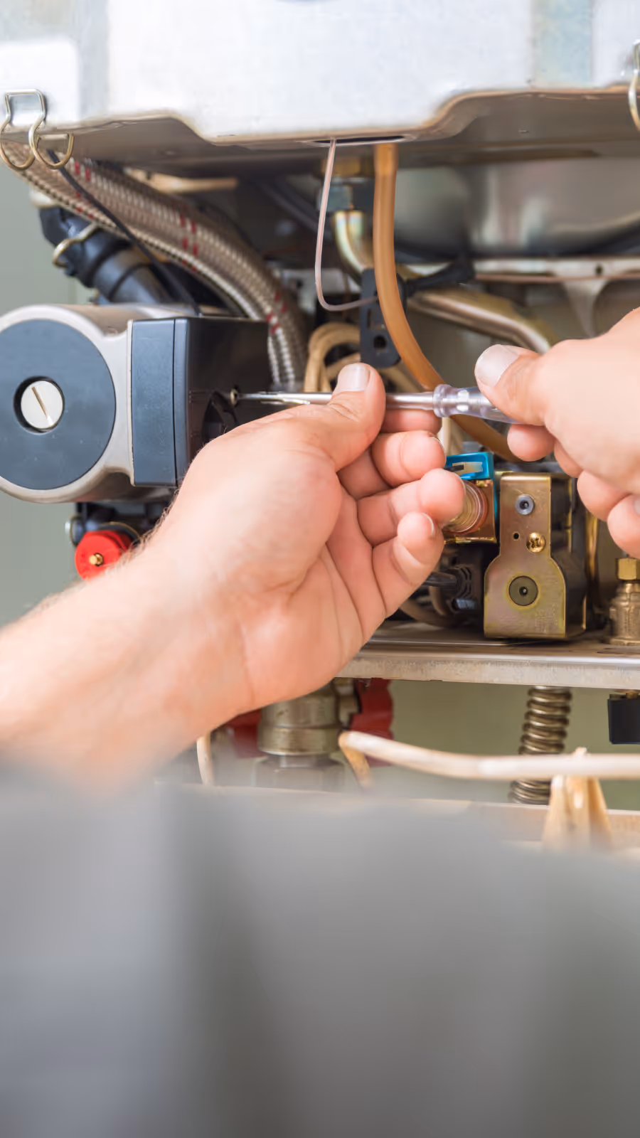 Hands using a screwdriver to repair the internal components of a furnace or heating system.