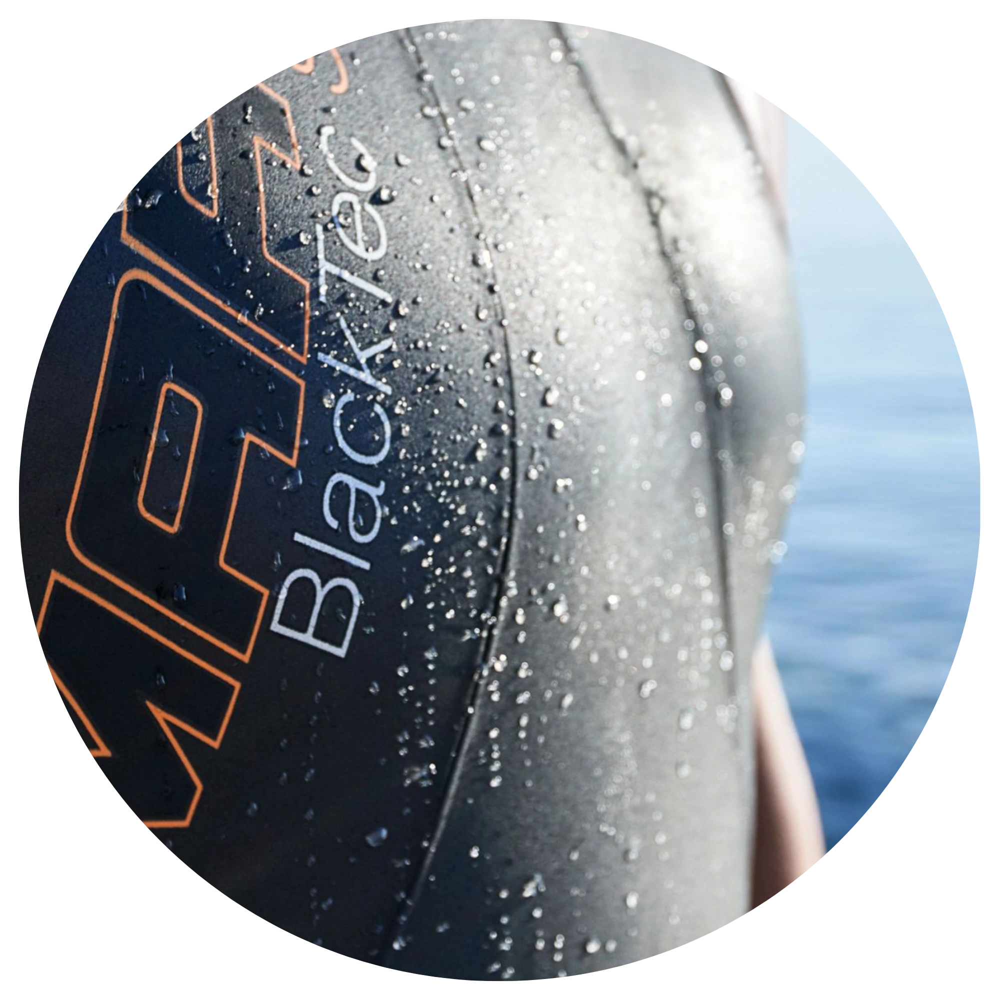 Close-up of a wet Blacktec wetsuit with water droplets against a blurred blue ocean background.