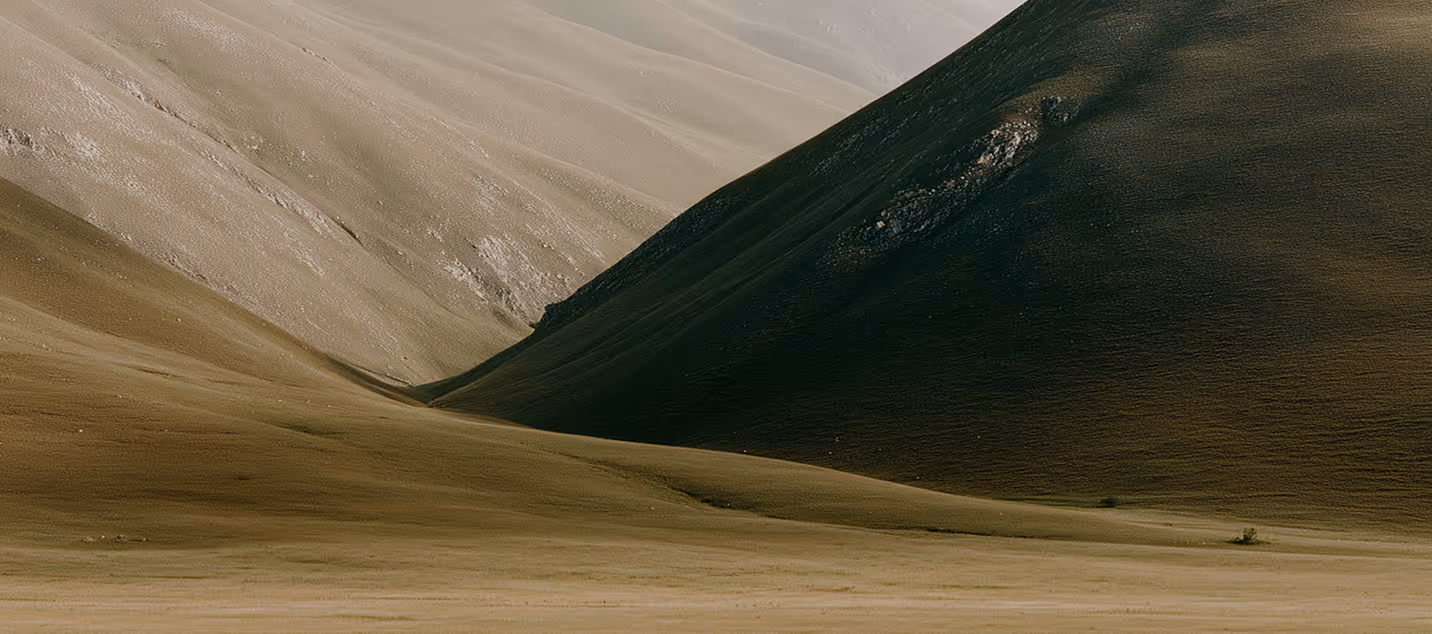 Gentle rolling hills with dry grass under soft lighting, showing contrast between light and shadow.