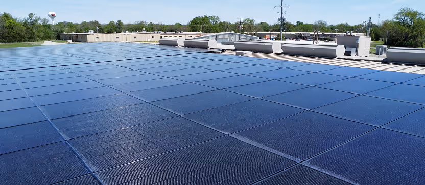 Rooftop covered with solar panels under a clear sky with trees and buildings in the background.