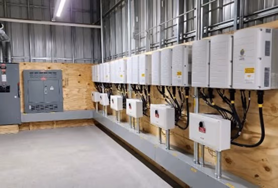 Row of white electrical inverter units mounted on a wooden wall inside an industrial facility.