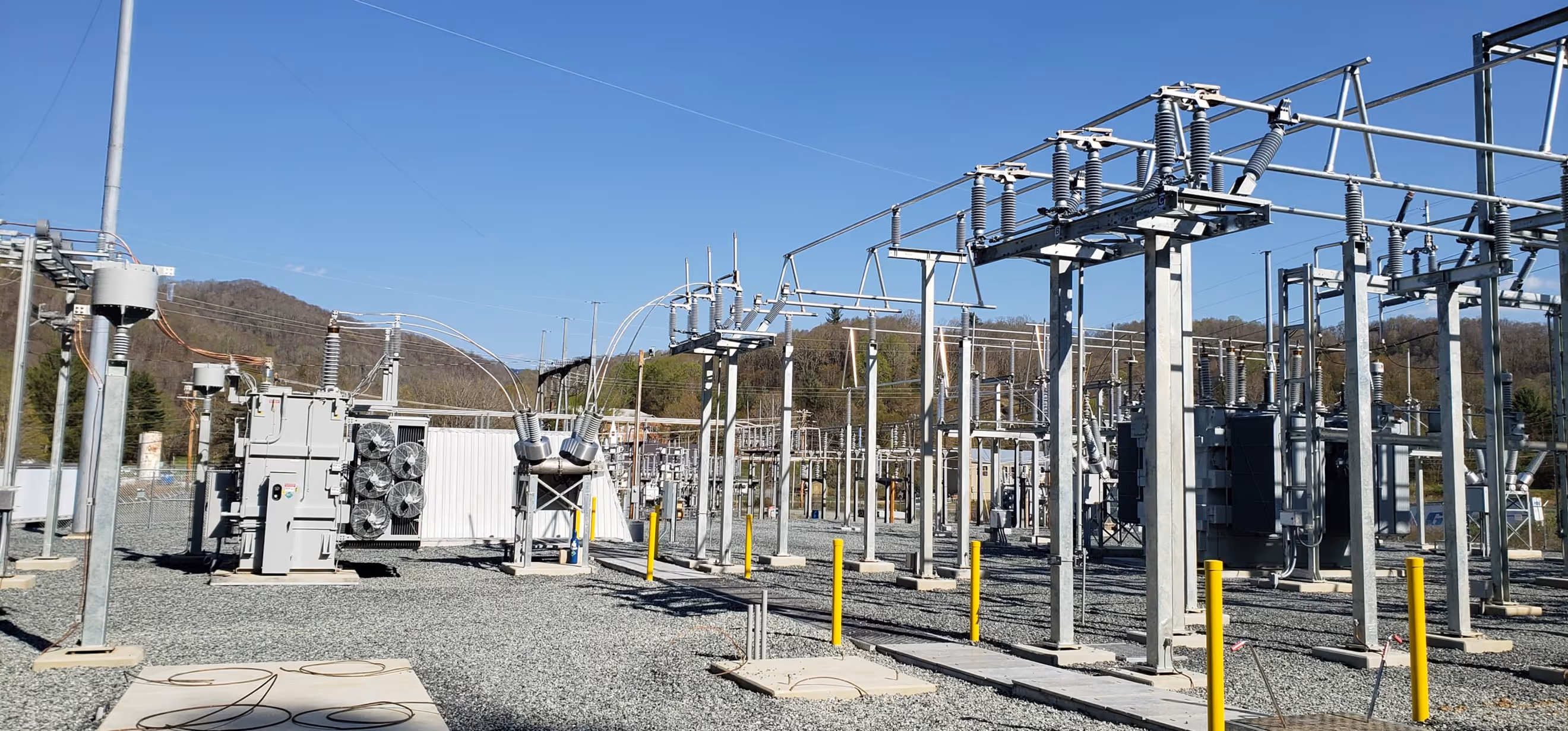 Electrical substation with transformers, insulators, and metal support structures under a clear blue sky.