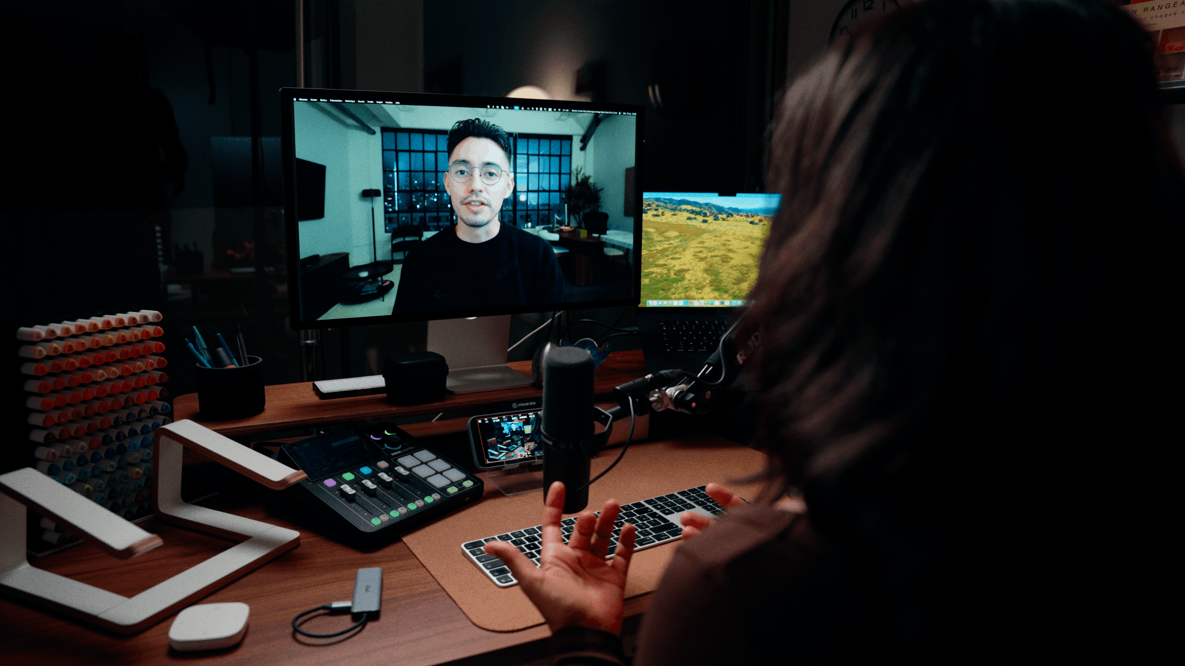 Man wearing a cap and sweater working on a laptop at a wooden table in a modern kitchen.