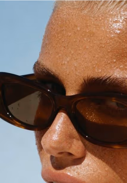 Close-up van een persoon met druppels water op het gezicht en donkerbruine zonnebril.