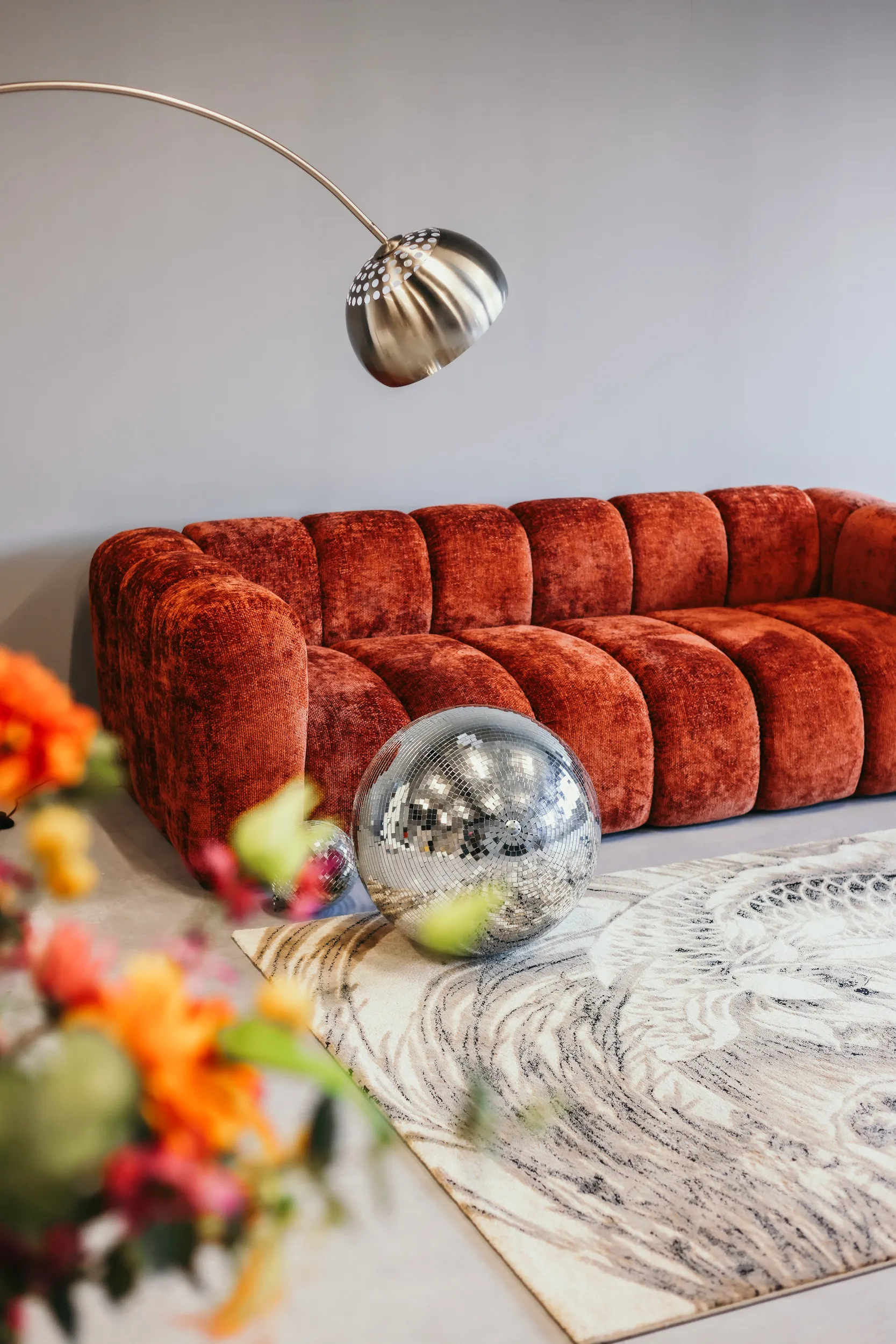 Rode geborgde stoffen bank met zilveren discobal en hanglamp in een moderne woonkamer.