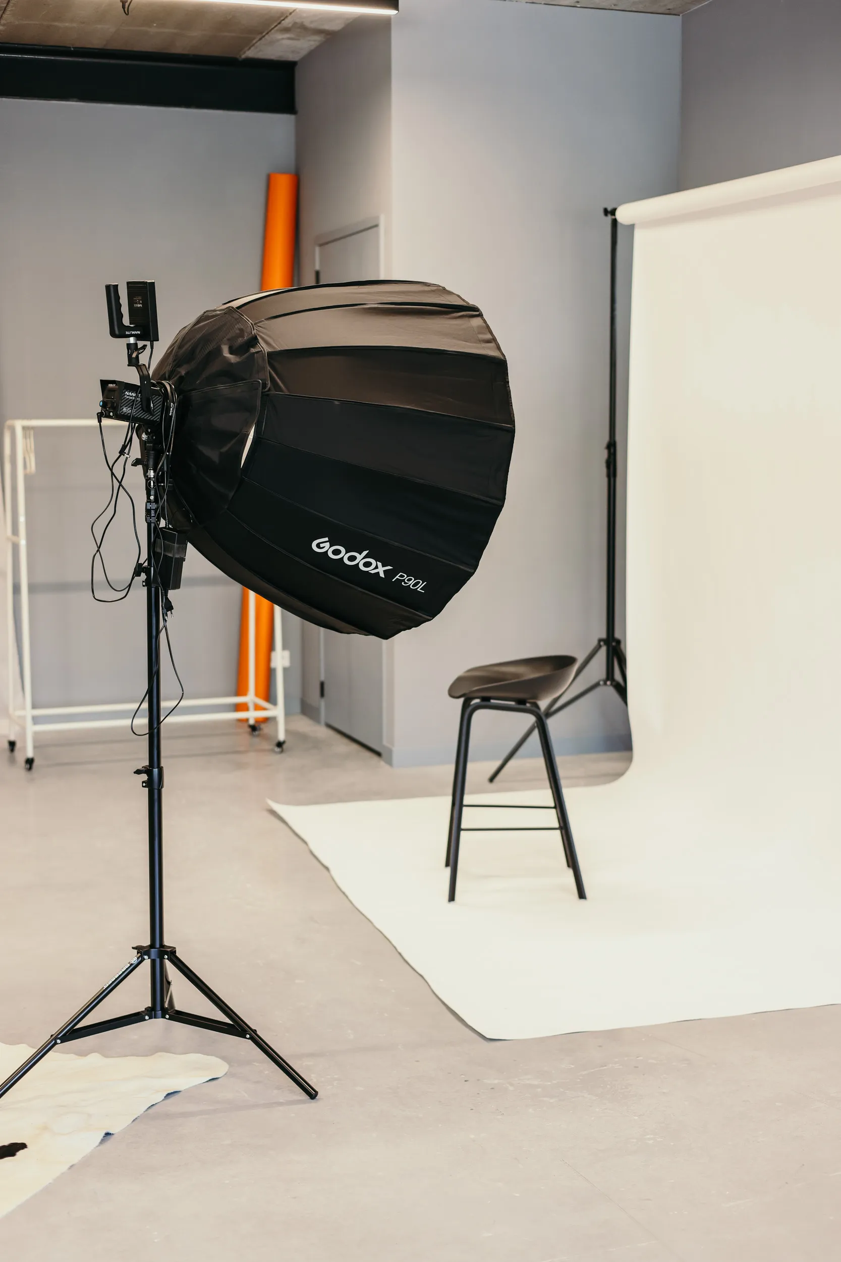 Fotostudio met een zwarte stoel voor een witte achtergrond en een grote Godox P90L softbox op een statief.