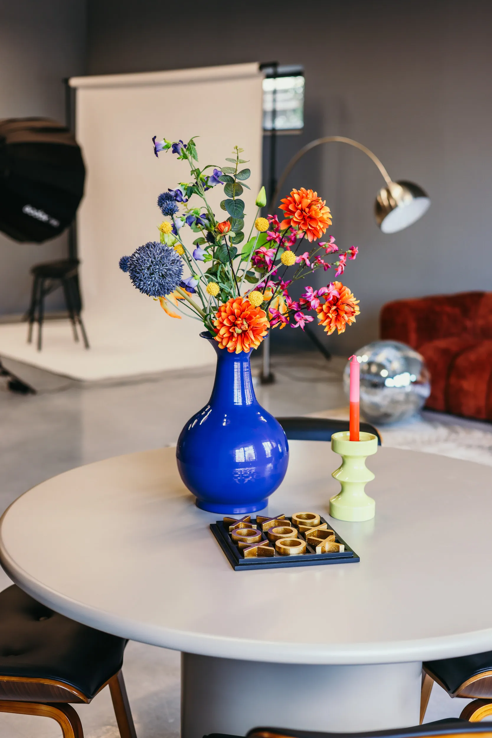 Ronde tafel met een blauwe vaas met kleurrijke bloemen, een groene kandelaar met een kaars en een bovenspel op een moderne kamerachtergrond.