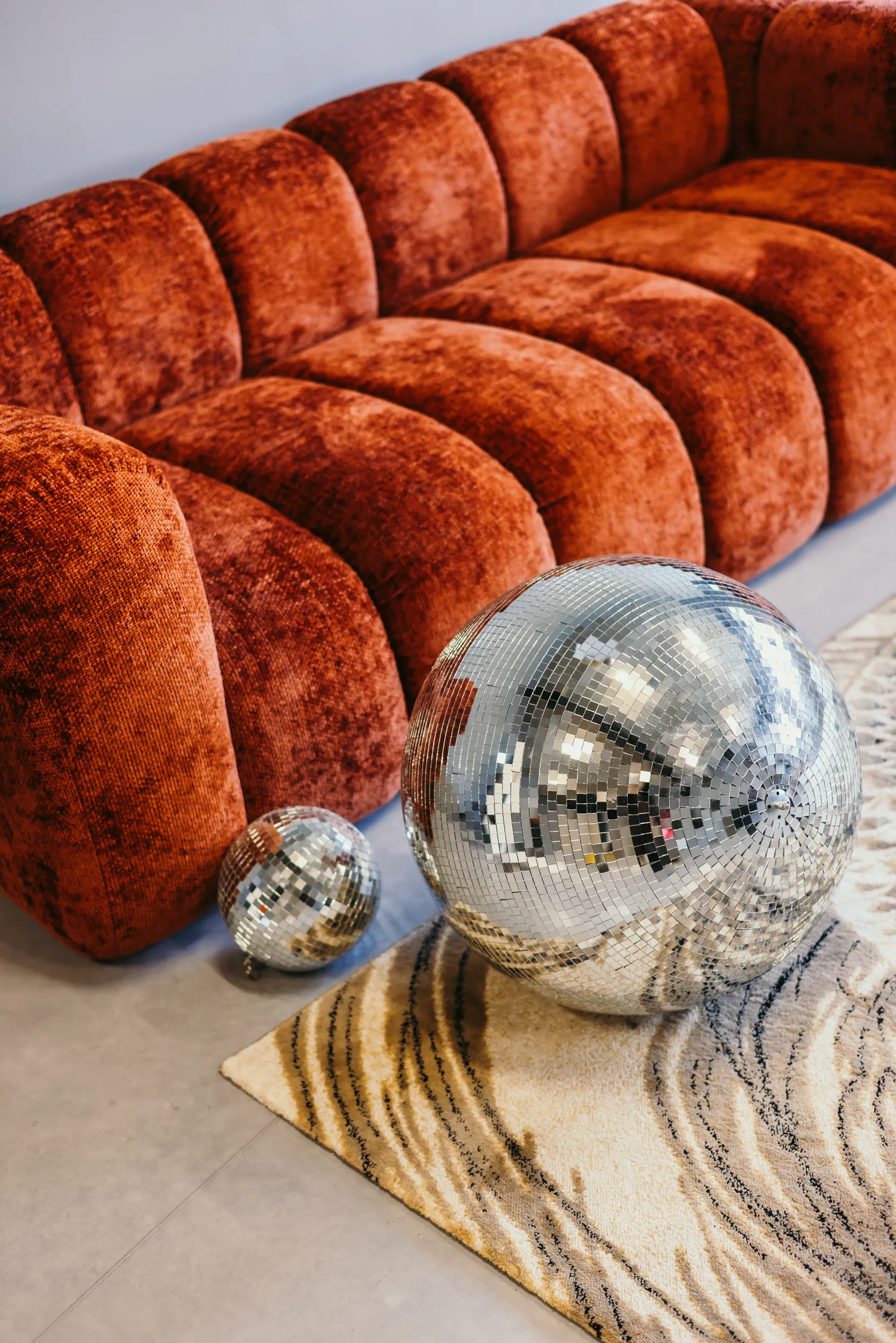 Rode fluwelen bank met twee glimmende discoballen op een beige vloerkleed met golvende patronen.