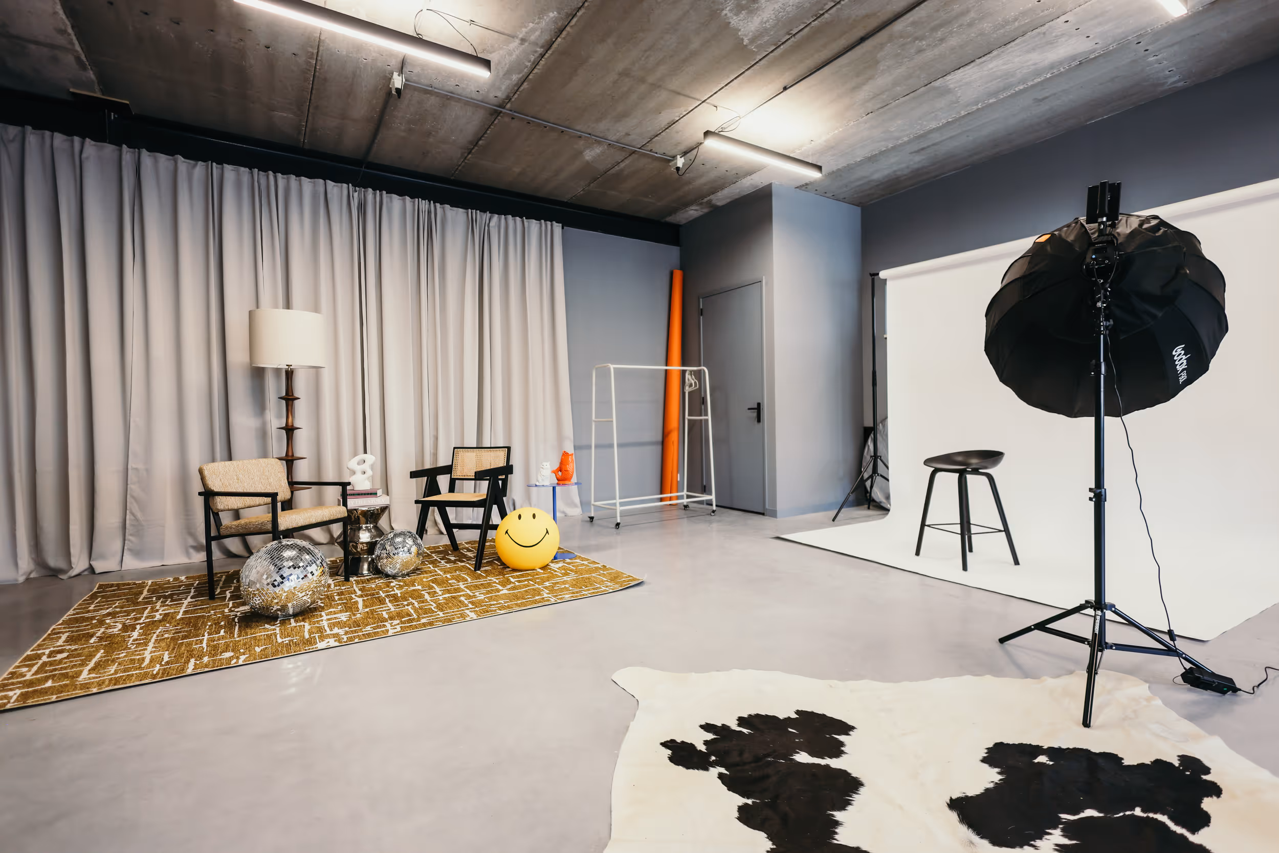 Fotostudio met twee stoelen, lachend gele bal, discoballen en lamp met witte achtergrond en zwarte kruk.