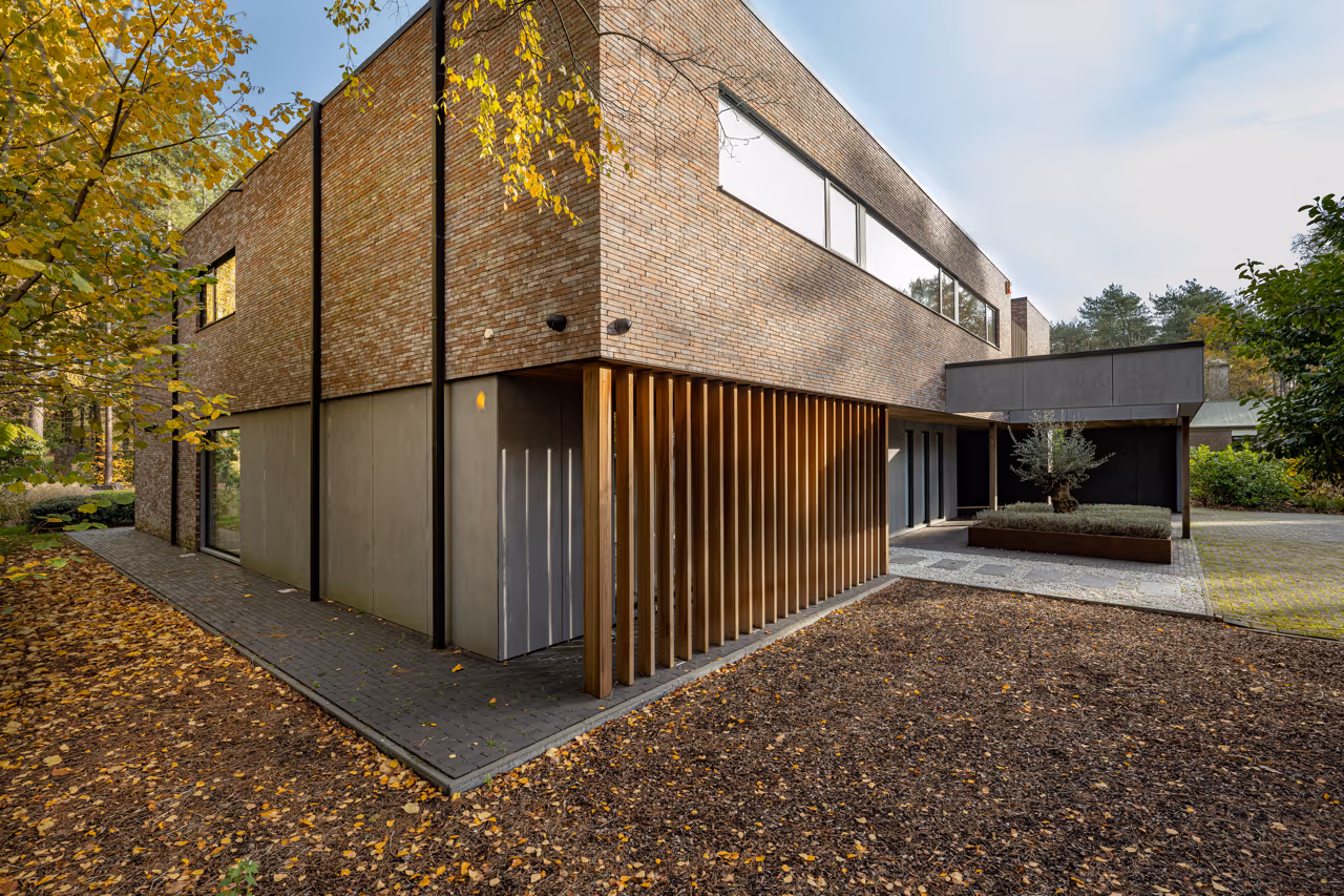 Moderne bakstenen woning met houten lattenwand en plat dak in een bosrijke omgeving