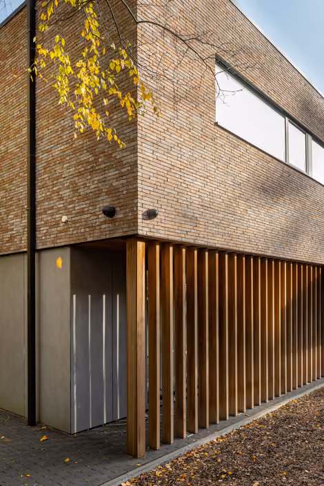 Detail van een bakstenen gevel met verticale houten lattenwand langs een moderne woning