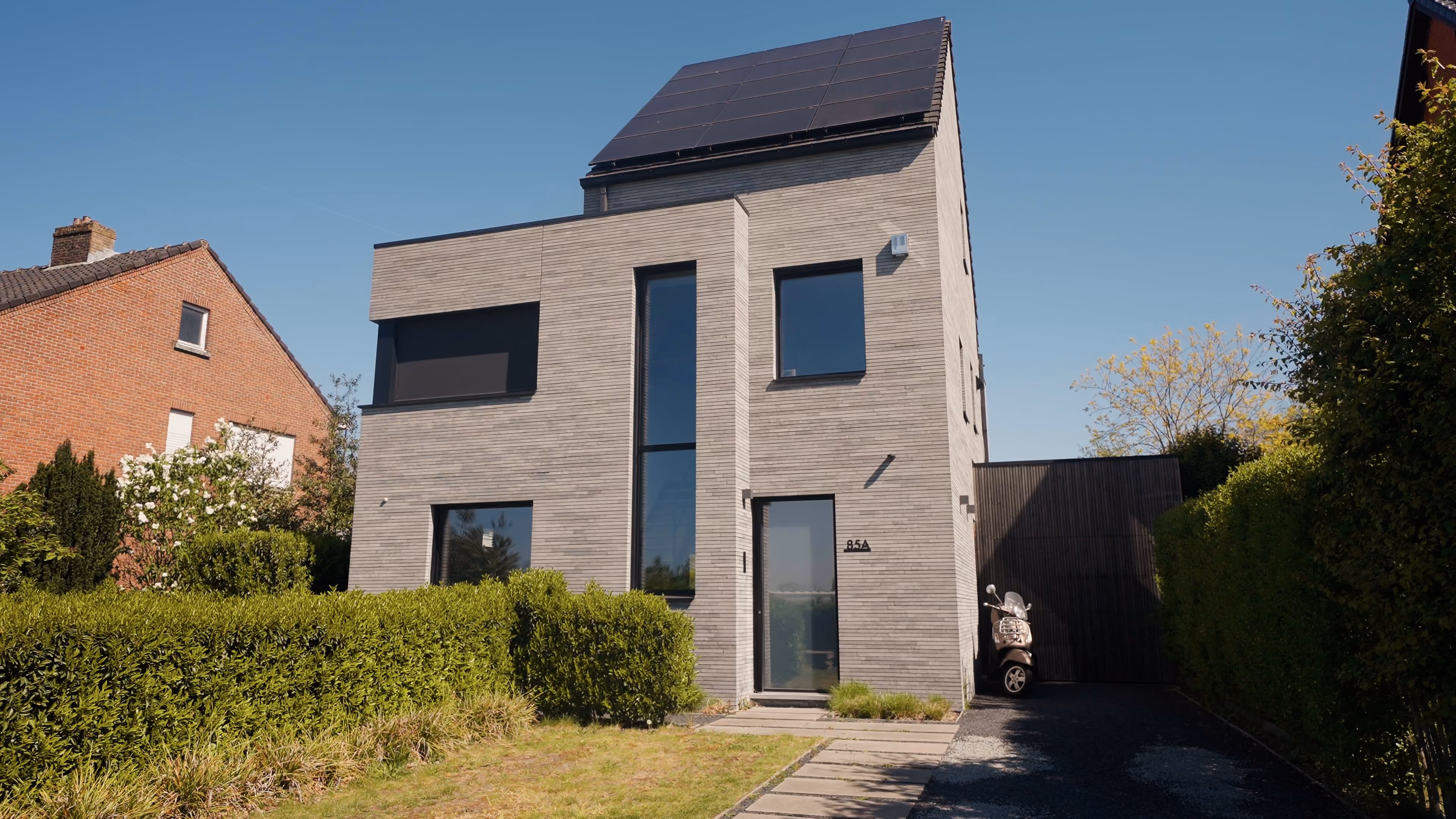 Vrijstaande nieuwbouwwoning met donkergrijze gevelbekleding en zonnepanelen achter een haag