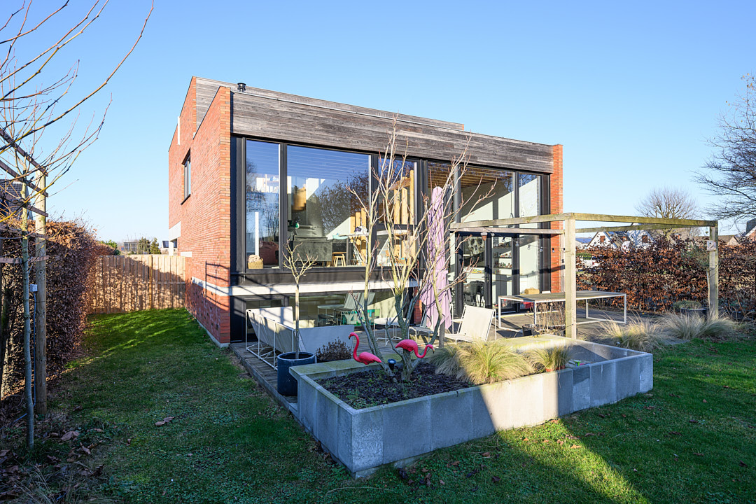 Tuinzijde van de passiefwoning met grote glaspartijen, terras en betonnen plantenbakken