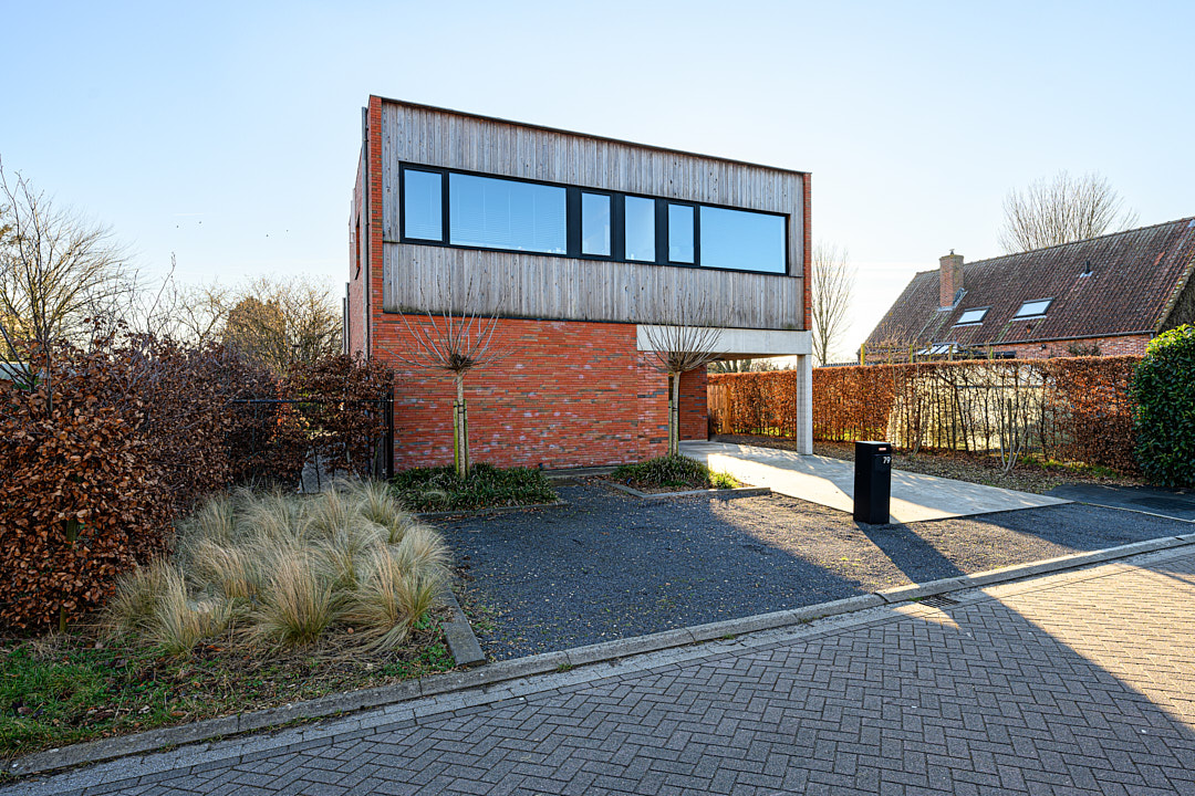 Straatzicht op de gezinswoning met bakstenen benedenverdieping en overkragend houten volume
