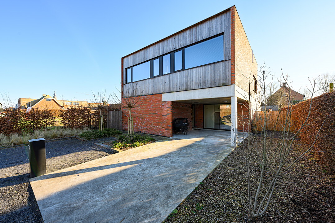 Passiefwoning in Hoogstraten met houten gevelbekleding, rode gevelsteen en carport onder de bovenverdieping