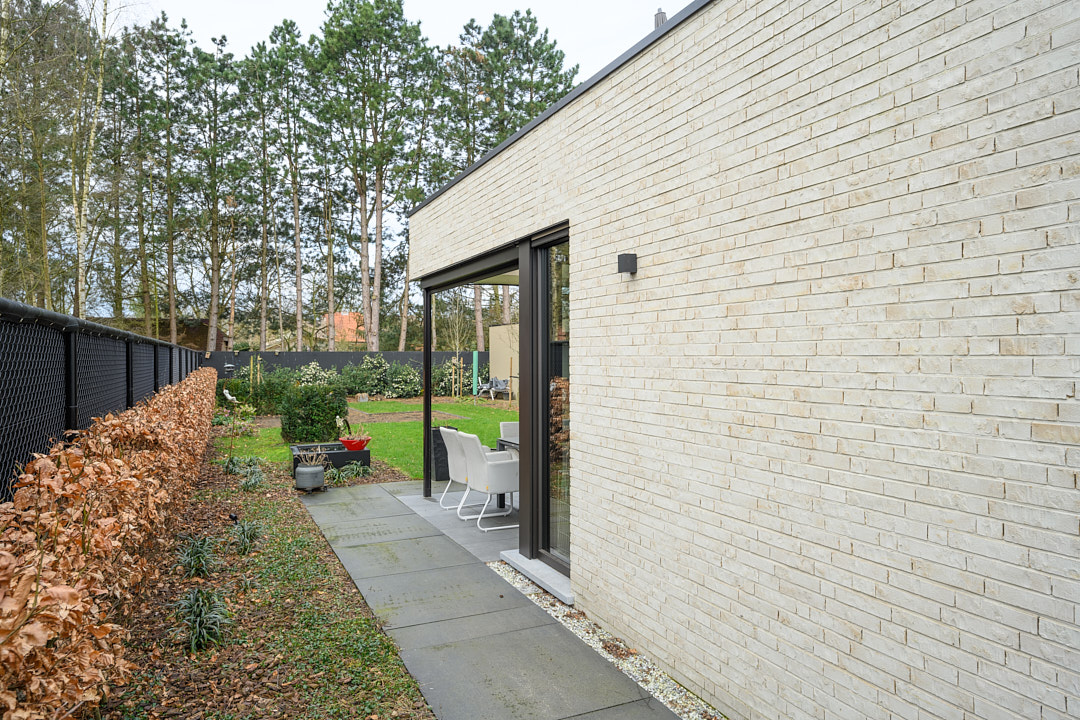 Zijpad langs de witte gevel naar het terras en de achtertuin van de woning in Beerse