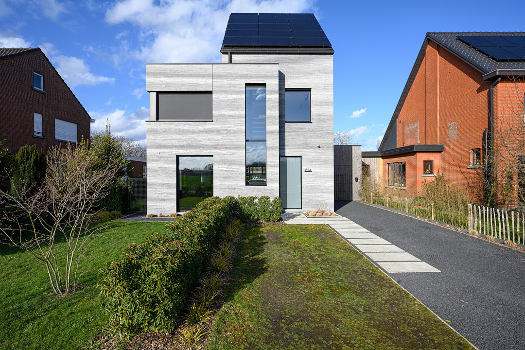 Compacte nieuwbouwvilla met lichtgrijze gevelsteen en zonnepanelen, met aangelegd voorpad en gazon