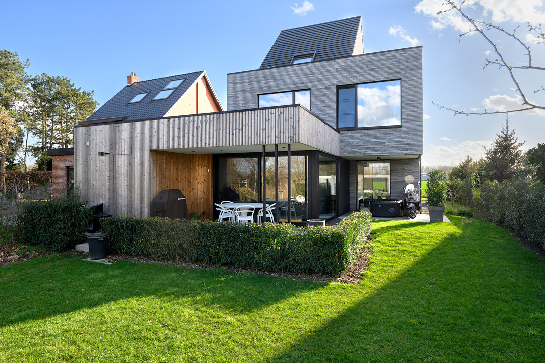 Tuinzijde met thermowood-gevelbekleding, ruime raampartijen en aangelegd terras achter een haag