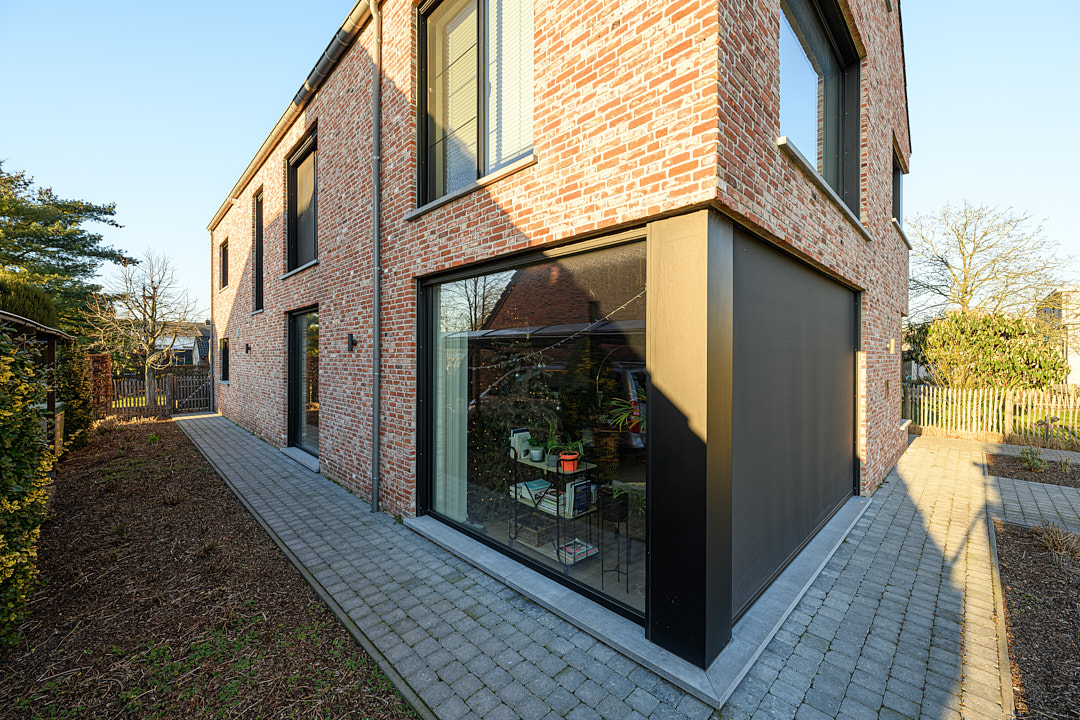 Zijgevel van de uitgebreide bakstenen woning met grote raampartijen en aangelegd terras