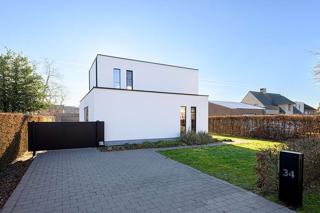 Achterzijde van de witte woning met opbouw, oprit en tuin na de verbouwing