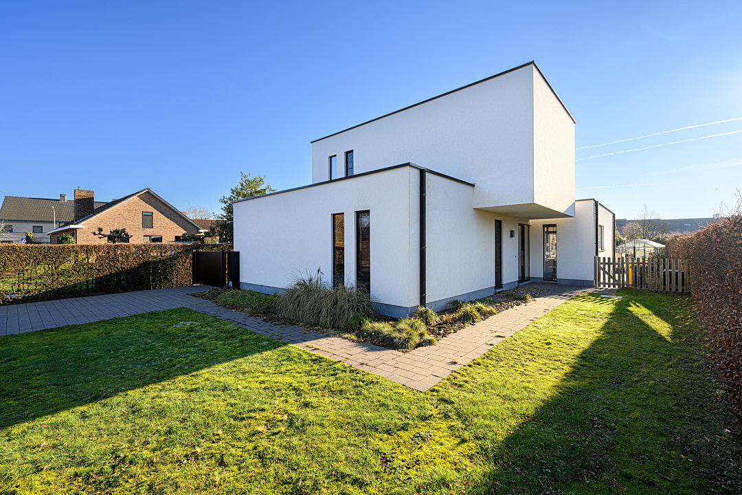 Zijaanzicht van de gerenoveerde witte woning met strakke crépi en verhoogd bouwvolume