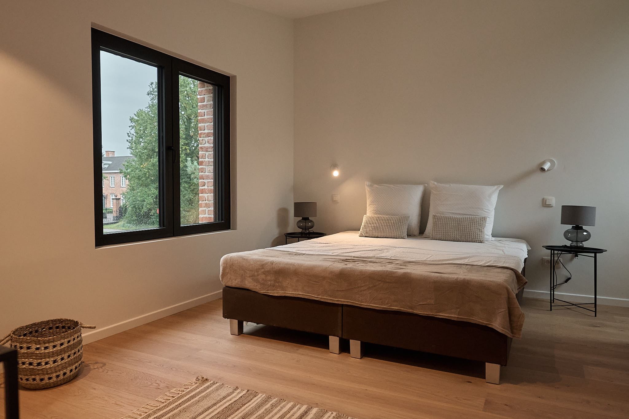 Lichte slaapkamer met boxspringbed, zwart raamkader en zicht op het groen buiten
