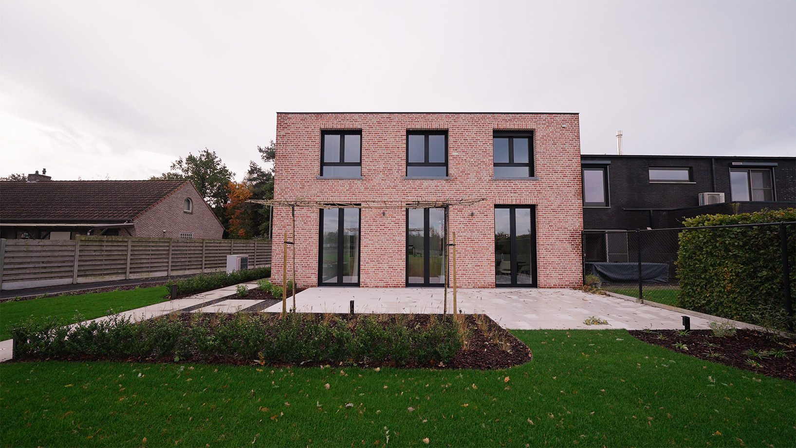 Achtergevel van de woning in Merksplas met rode gevelsteen, grote ramen, terras met pergola en tuin