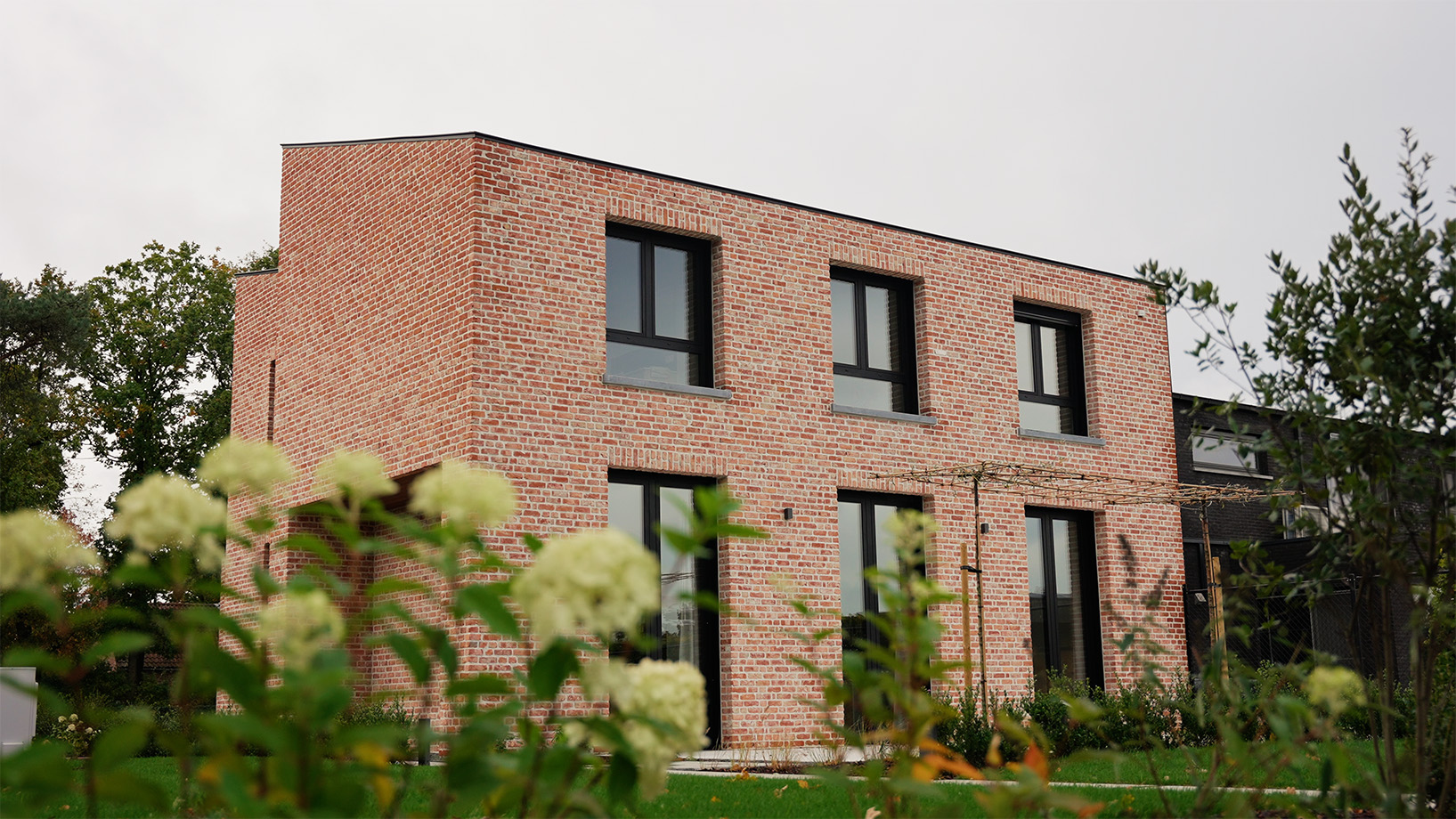 Rechthoekige nieuwbouwwoning in rood-genuanceerde gevelsteen achter bloeiende hortensia's