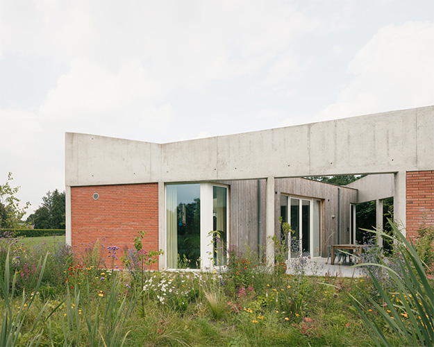 Achtergevel in baksteen en beton met glaspartijen achter een wilde tuinbeplanting