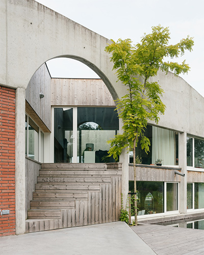 Betonnen boog boven een houten trap die naar de verhoogde leefruimte leidt