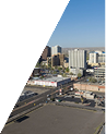 Cityscape view with tall buildings, roads, and parking areas under a clear sky.
