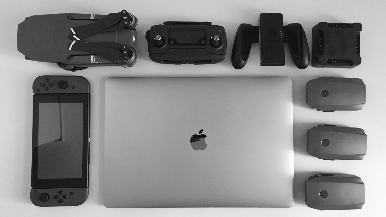 Alt text: Laptop, game console, drone, controllers, and batteries arranged from above.