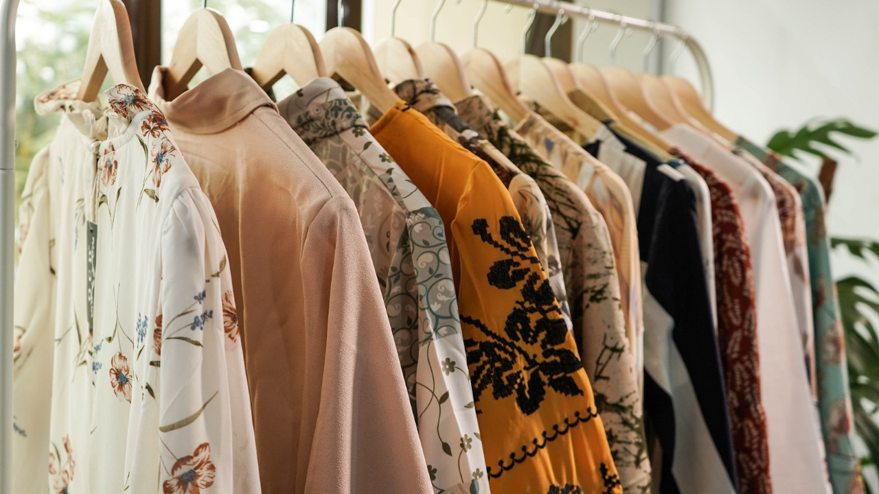 Alt text: Colorful blouses and dresses hanging on a wooden clothes rail.