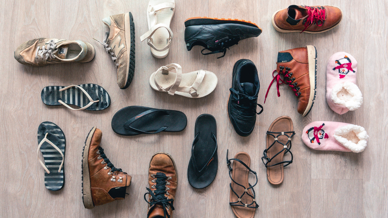 Alt text: Shoes, sandals, and slippers arranged across a wooden floor.