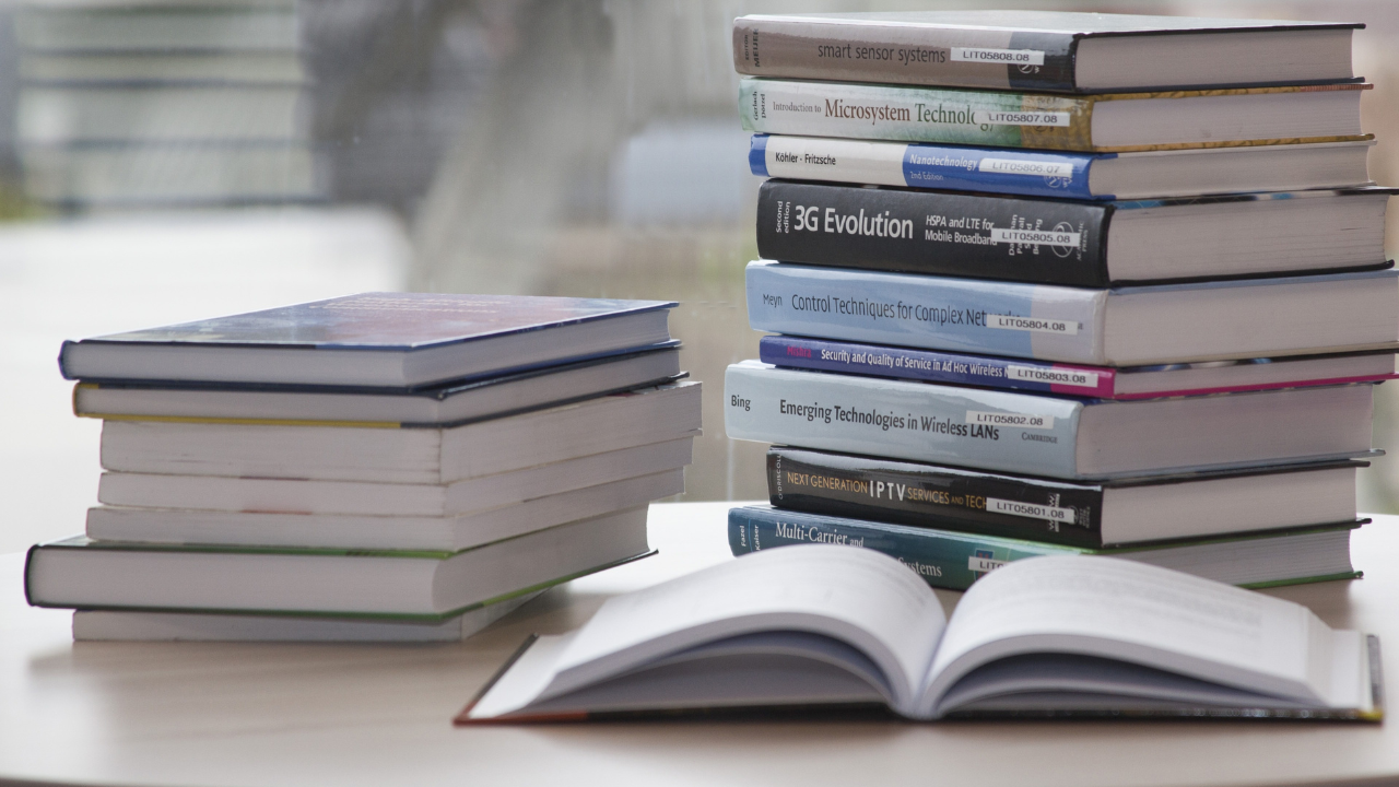 Alt text: Stacks of technical books beside an open book on a desk.