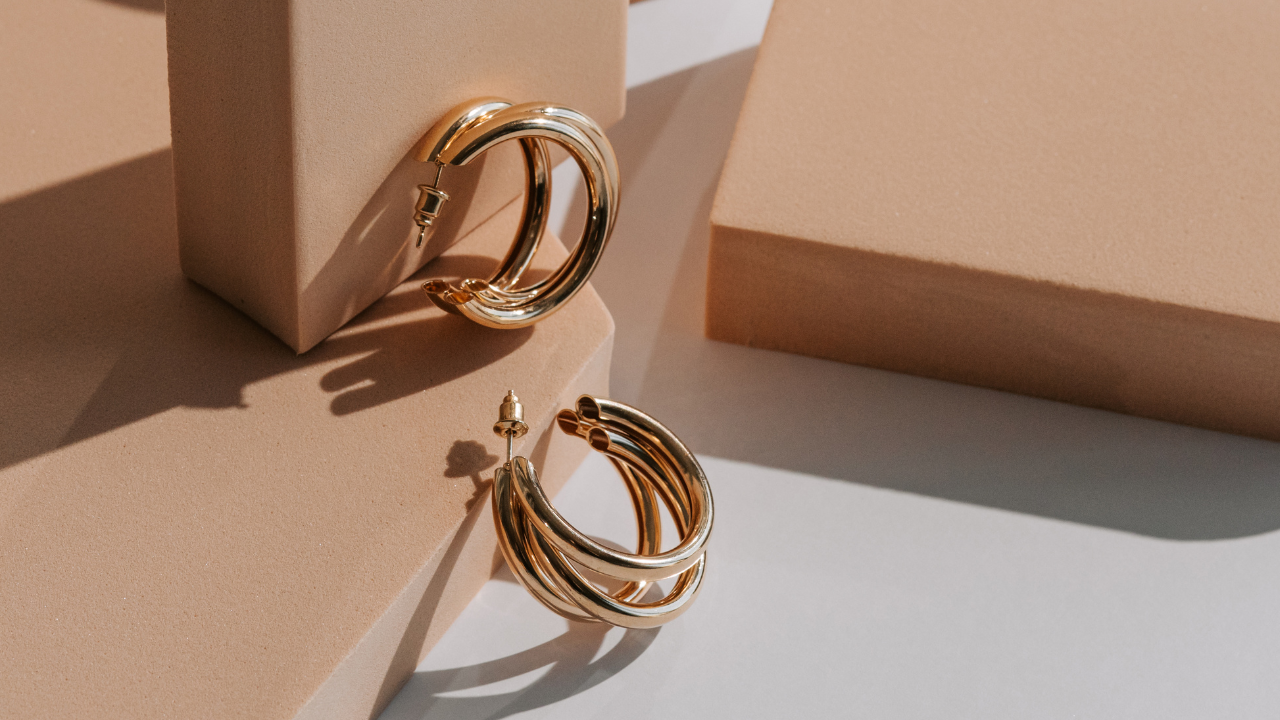 Two pairs of gold hoop earrings displayed on neutral blocks