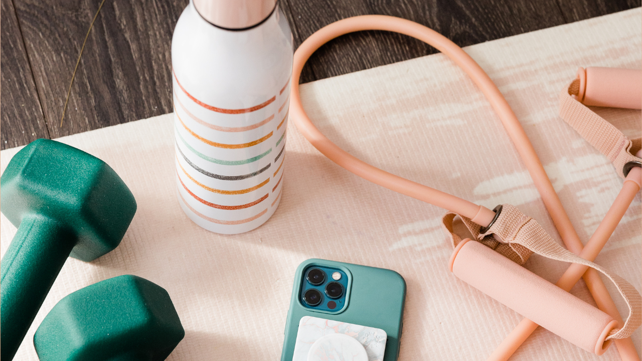 Green dumbbells, a resistance tube, a water bottle, and a phone on a workout mat