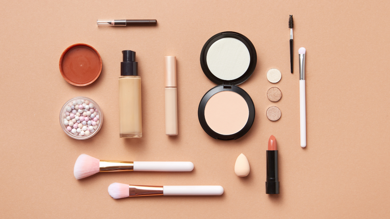 Makeup compacts, brushes, foundation, lipstick, and other beauty products on a peach background